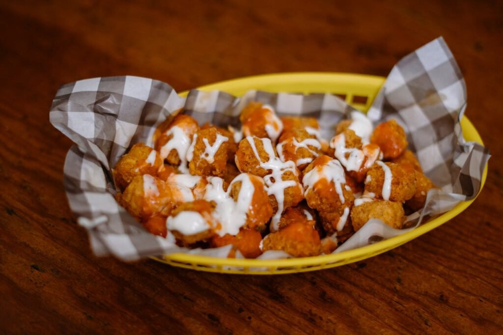 pexels-photo-32667559 Crispy tater tots topped with cheese and ranch dressing served in a basket.